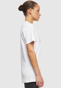 T-shirt en coton blanc à manches courtes, présentant un design simple et un col rond classique. La vue de côté montre une coupe décontractée et une texture lisse.