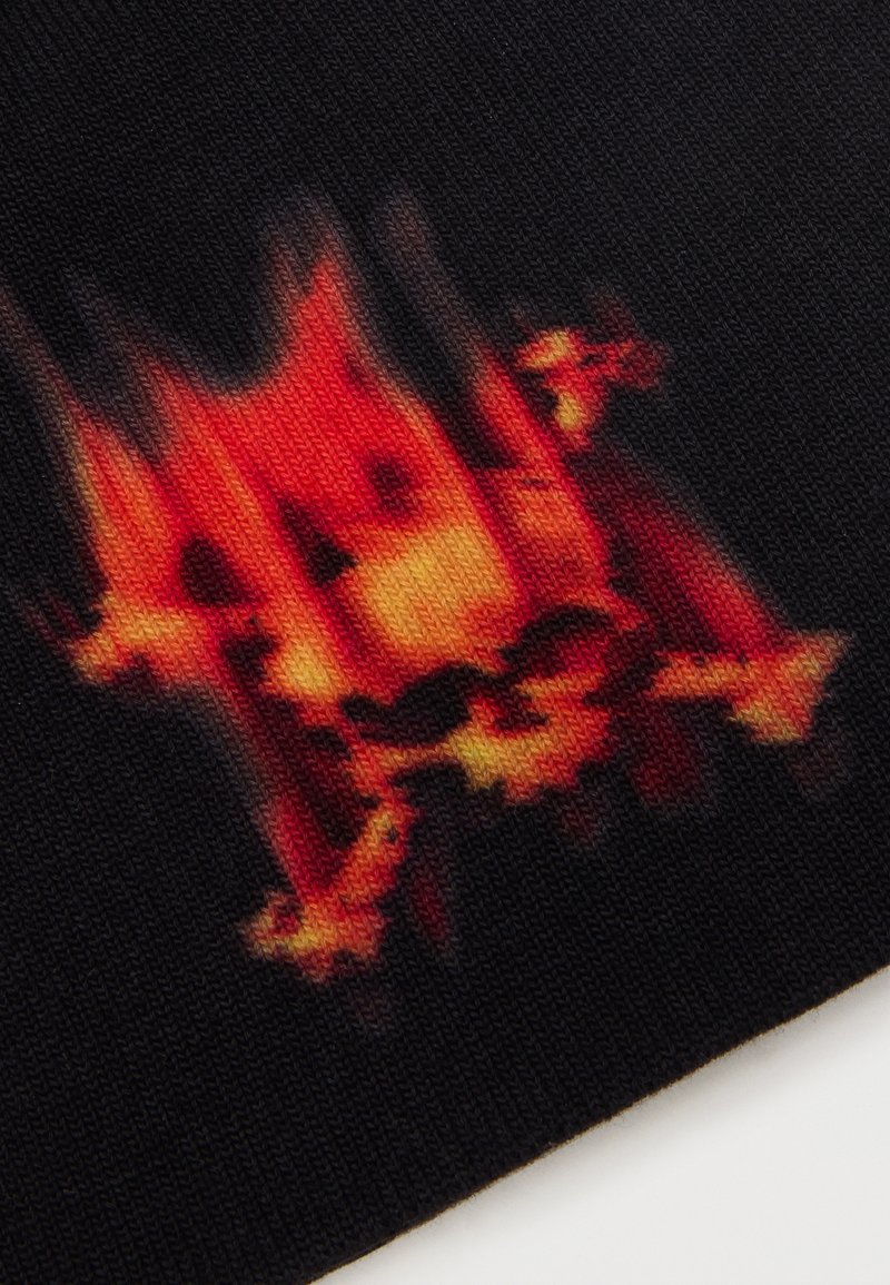 Crâne rouge flamboyant et orange avec un motif de tibias croisés sur un tissu tricoté noir.