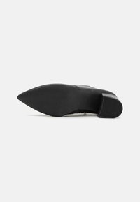 Zapato de tacón alto negro con punta afilada y suela texturizada, con un diseño superior liso y un tacón cuadrado.