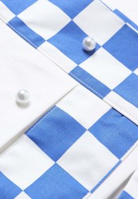 Gros plan d’un tissu à carreaux bleu et blanc avec des poignets blancs ornés de boutons ronds en perle.