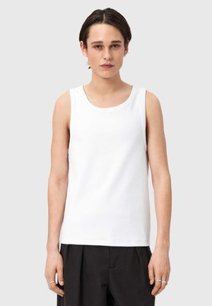 Biały bawełniany tank top z okrągłym dekoltem i szerokimi otworami na ramiona; gładka faktura; noszony z czarnymi, luźnymi spodniami.