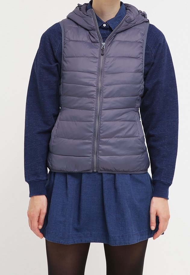 Gepolsterte ärmellose Weste in Dunkelgrau mit Kapuze, ausgestattet mit einem Frontreißverschluss und gestepptem Design, getragen über einem blauen Langarmshirt und einem Rock.