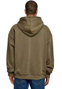 Hanorac supradimensionat de culoare verde măslinie, cu glugă mare, mâneci largi și tiv cu dungi. Material texturat, croi lejer și detalii minime.