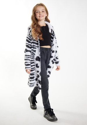 Műszőrme kabát fekete csíkokkal és pöttyökkel, fekete gumis derekú nadrággal és fekete magas szárú tornacipővel párosítva.