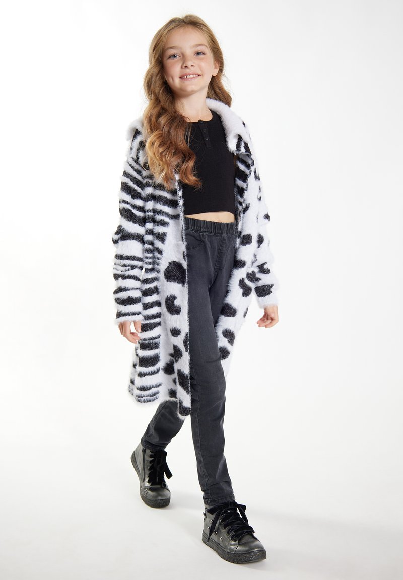 Faux fur-kappa med svarta ränder och prickar, kombinerad med svarta byxor med elastisk midja och svarta hög-top sneakers.