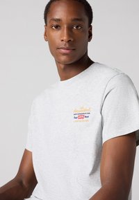 Grijze katoenen t-shirt met korte mouwen, met kleurrijke geborduurde branding op de borst, een gladde textuur en een ronde halslijn.