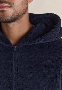 Granatowa polarowa bluza z kapturem na zamek błyskawiczny o miękkiej, textured powierzchni i przestronnym kapturze, z czarnym zamkiem z przodu.