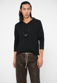 Črna majica dolgimi rokavi z V-izrezom in štirimi gumbi, v kombinaciji s svetlo rjavimi usnjenimi hlačami z belim vrvico. Minimalističen črn etui.