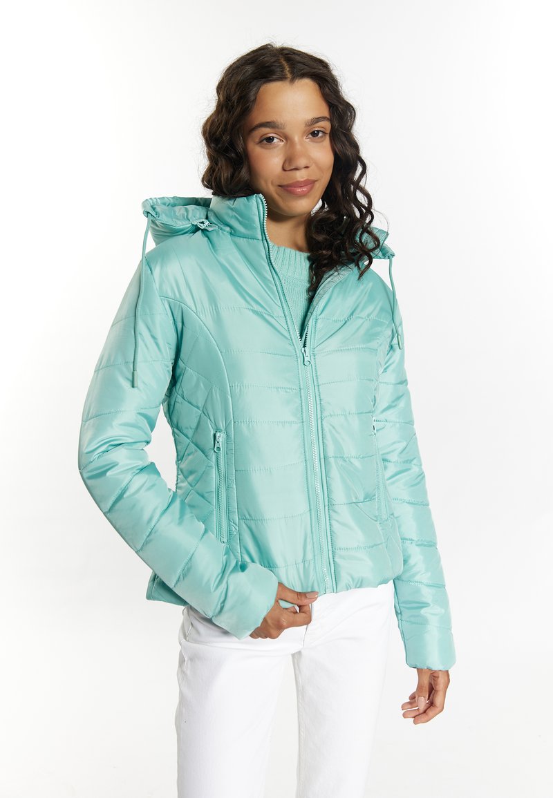 Geacă puf light teal cu fermoar frontal, două buzunare laterale și glugă. Prezintă un model matlasat și o textură netedă. Asortată cu pantaloni albi.