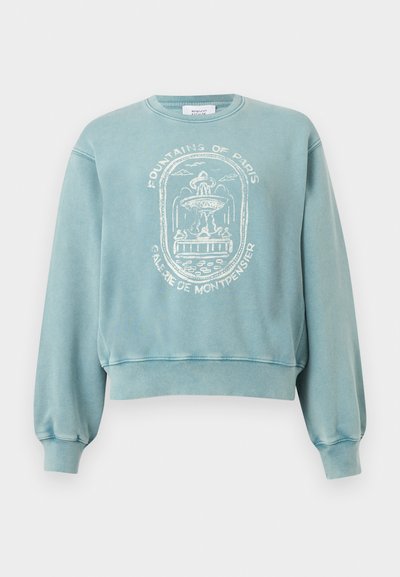 Ανοιχτό μπλε φούτερ με ριμπ μανσέτες και τελείωμα, με λευκό γραφικό μιας συντριβανιού του Παρισιού και το κείμενο «Fountains of Paris Galerie de Montpensier».