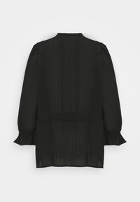 Blouse noire à manches longues en tissu texturé, présentant une silhouette ample, des poignets froncés et une taille cintrée.