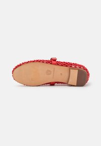 Nu-pieds tressés rouges avec une semelle plate, présentant une bride décorative et un coussin en cuir tan. Comprend un petit détail de boucle.