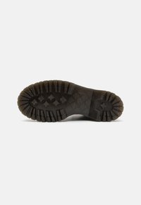 Suela de bota de goma negra con un patrón de tracción profundo, formas hexagonales y estrelladas, superficie texturizada y área de punta redondeada.