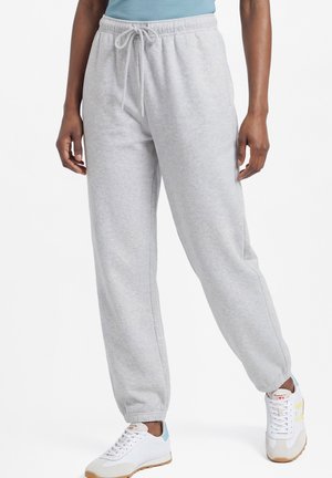 Persoon die lichtgrijze joggingbroek draagt met elastische manchetten en een taillekoord, gecombineerd met witte sneakers en een lichtblauw topje.