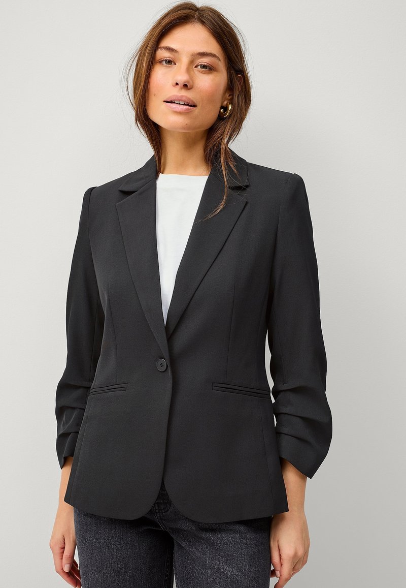 Zwarte op maat gemaakte blazer met een enkele knoopsluiting, notch-revers en twee zijzakken. Gemaakt van een gladde stof, met lichtgeplooide mouwen.