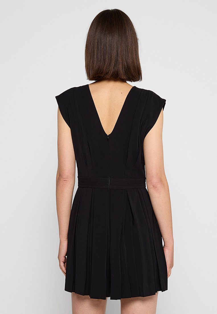 Schwarzes Kleid mit V-Ausschnitt, kurzen Ärmeln und plissiertem Rock. Hergestellt aus einem strukturierten Stoff, mit einem diskreten Reißverschlussverschluss auf der Rückseite.