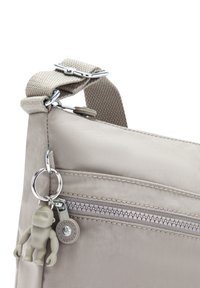 Light beige crossbody bag with a textured fabric, adjustable strap, front zip pocket, and a keychain featuring a small toy figure.