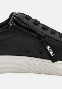 Baskets en cuir noir avec lacets noirs, fermeture éclair latérale et languette noire portant l'inscription "BOSS", semelle blanche texturée.