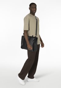 Bolso mensajero de cuero negro con forma plana, asas superiores y correa de hombro ajustable. Textura suave y diseño minimalista.
