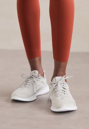 Weiße Sportschuhe mit einer strukturierten Strick-Oberfläche, Schnürsystem und Nike-Swoosh-Logo, kombiniert mit eng anliegenden rötlich-braunen Leggings.