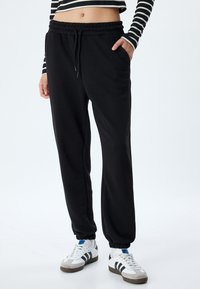 Schwarze Jogginghose mit elastischem Bund und Kordelzug. Mit Seitentaschen und taillierten Bündchen. Weiches Material mit glatter Textur.