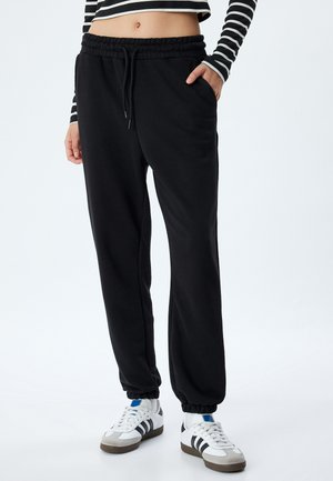 Zwarte sweatpants met een elastische tailleband en trekkoord. Voorzien van zijzakken en taps toelopende boorden. Zacht materiaal met een gladde textuur.