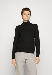 Pull à col roulé noir en tissu lisse, doté de manches longues et d'une silhouette ajustée, associé à un pantalon gris clair.