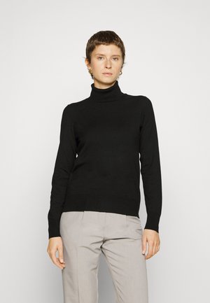 Schwarzer Rollkragenpullover aus glattem Stoff, mit langen Ärmeln und einer taillierten Silhouette, kombiniert mit hellgrauen Hosen.