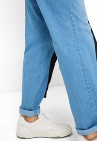 Light blue denim jeans with rolled cuffs, paired with white sneakers. The jeans feature a smooth texture and classic five-pocket design.