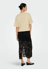 Beige cropped t-shirt, oversized pasvorm, gecombineerd met een zwarte kanten rok met bloemmotieven en zijsplitten. Zwarte flats maken de outfit compleet.