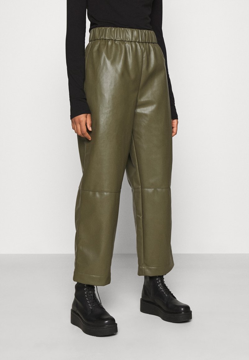 Pantaloni in ecopelle verde oliva con vita elastica, gamba larga e cuciture visibili, abbinati a stivali militari neri con lacci.