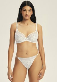 Weißes Spitzen-Unterwäsche-Set mit einem Balconette-BH mit gezackten Kanten und passendem String. Zarte Blumenmuster überall.