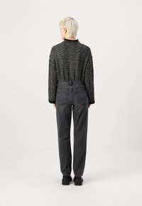 Schwarz-weißer gestrickter Pullover mit Muster und langen Ärmeln, kombiniert mit grauen hochtaillierten Jeans und schwarzen Plateauschuhen.