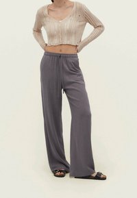 Beige korte cardigan met geprofileerde strepen en knopen, gecombineerd met losse, grijze wijde broek met een elastische tailleband en trekkoord.