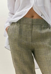 Vihreät ja keltaiset houndstooth-kuosiset housut, jotka on valmistettu teksturoidusta kankaasta, ja niissä on tasainen etuosa, sivutaskut ja elastinen vyötärönauha.