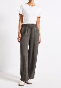 Lehká, plisovaná, olivově zelená kalhoty s elastickým pasem, spárované se jednoduchým bílým tričkem a krémovými teniskami.