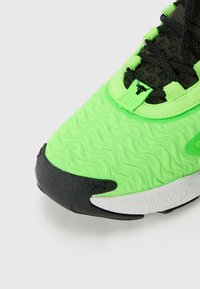 Scarpa sportiva verde con upper testurizzato, accenti neri e suola bianca con un design a motivo. Dettaglio del logo presente in evidenza.