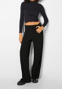 Zwarte broek met wijde pijpen, een gladde textuur, hoge taille, sluiting met een frontknop en plooitjes, gecombineerd met een aansluitend ribgebreid shirt met lange mouwen.