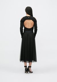 Melnas garām piedurknēm tops ar atvērtu muguras dizainu, kombinēts ar melnu tilla svārku ar spīdīgām detaļām un potītes siksniņu augstpapēžu kurpēm.