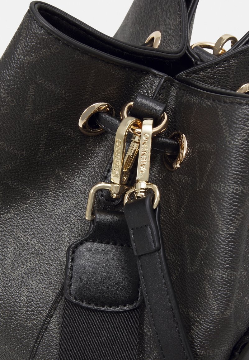 Černá texturovaná kožená taška se zlatými detaily. Obsahuje zavírání na šňůrku, metalické akcenty a odnímatelný popruh.