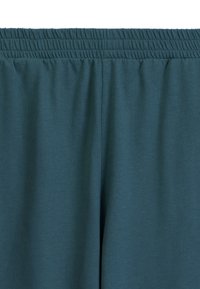 Turkusowe dresy bawełniane z elastycznym pasem. Gładka tekstura, marszczone detale w pasie i luźny krój.