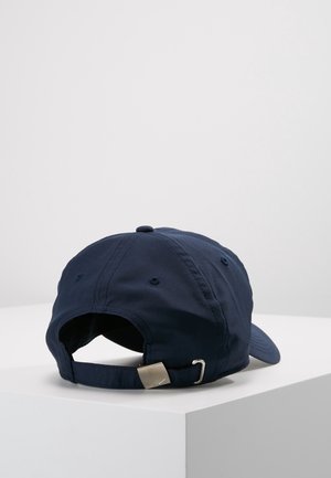 Casquette de baseball bleu marine avec sangle à boucle métallique réglable reposant sur une surface blanche, vue de dos.