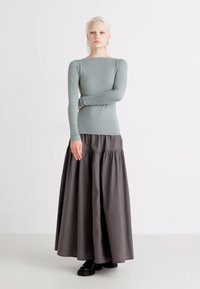 Long-sleeve, light green top paired with a dark gray, ankle-length skirt featuring a gathered waistline, worn with black footwear.
