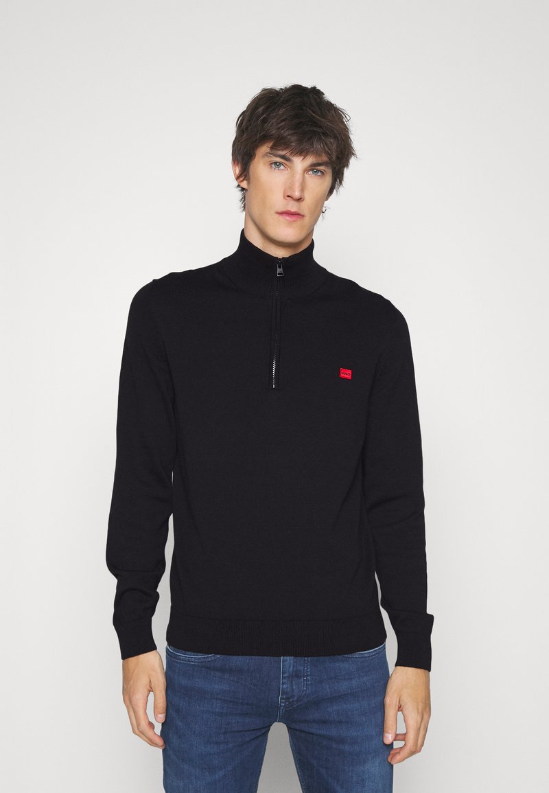 Schwarzer Zip-Pullover mit langen Ärmeln, gerippten Ärmelbündchen und Saum, mit einem kleinen roten Logo auf der Brust. Weicher Strickstoff.
