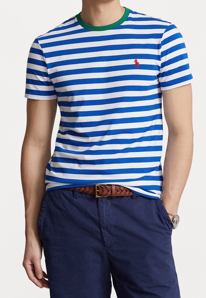 Pruhované modro-bílé tričko s zeleným límcem, na hrudi s malým červeným logem. Nosené s námořnickými šortkami a hnědým pleteným opaskem.