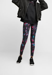 Svarta leggings med en flerfärgad abstrakt design i rosa och turkos. Bärs med en svart hoodie och bomberjacka, tillsammans med svarta skor.
