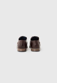 Zapatos de cuero marrón con punta redondeada, tacón bajo y acabado suave. Presentan una ligera textura y una suela de madera marrón.