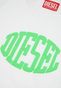 T-shirt in cotone bianco con lettering bold e verde brillante "DIESEL". L'etichetta all'collo recita "DIESEL PER UNA VITA DI SUCCESSO."
