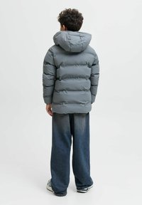 Grå puffjacka med huva, med en kviltad design och elastiska manschetter, tillsammans med löst sittande mörka jeans.
