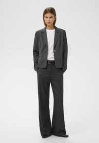 Gray tailored blazer with a single button, paired with wide-leg gray trousers and a white t-shirt. Smooth texture, structured design.